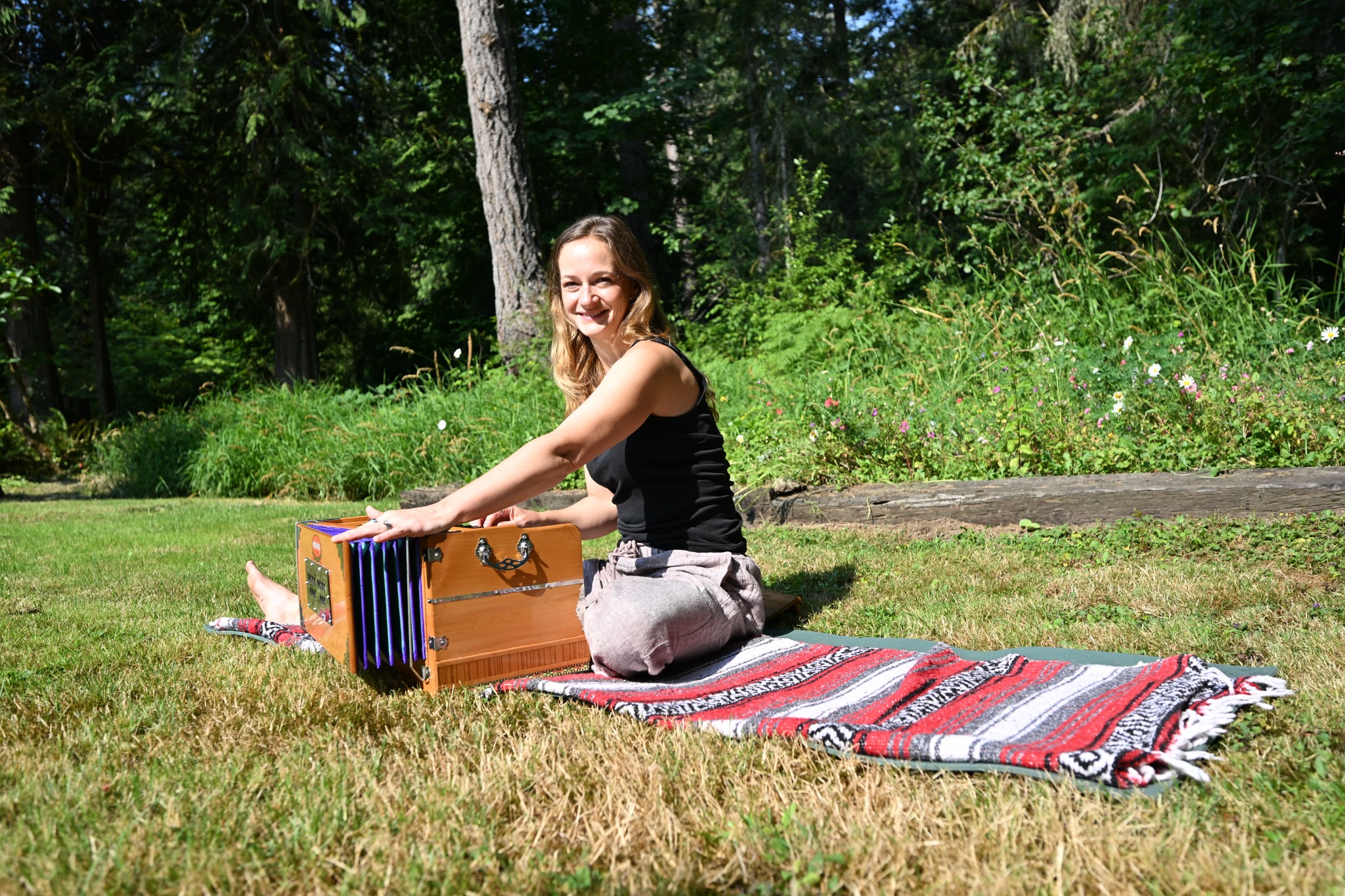 Jess smiling beside her harmonium in a sunny Pacific Northwest garden